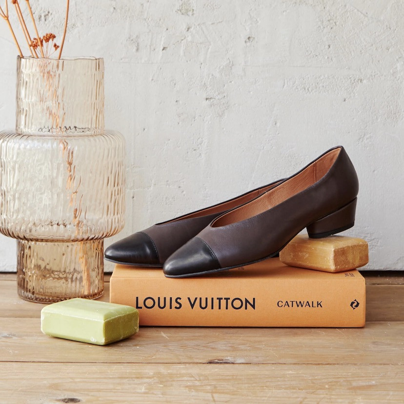 Brown leather ballerina with bicolor toe and heel, angled view, resting on a book and soap - MONPIEL