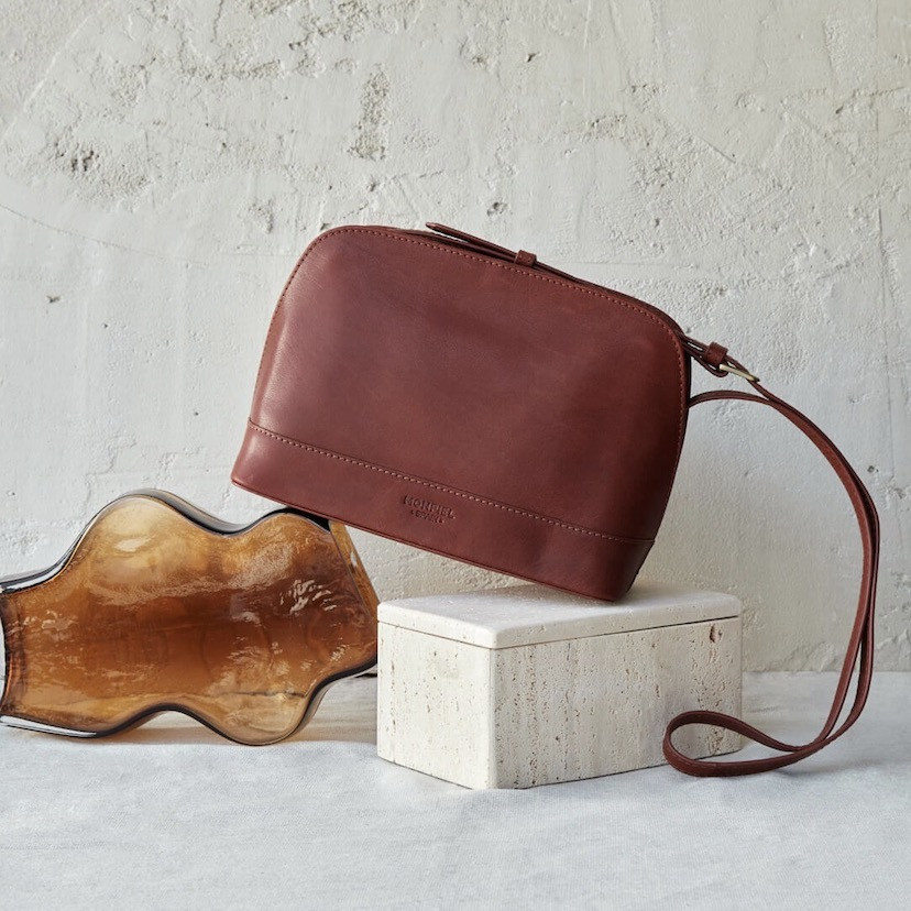 Medium leather bag in tan color, front view, tilted and resting on a vase - MONPIEL