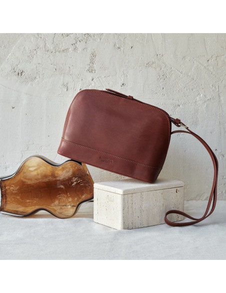Medium leather bag in tan color, front view, tilted and resting on a vase - MONPIEL