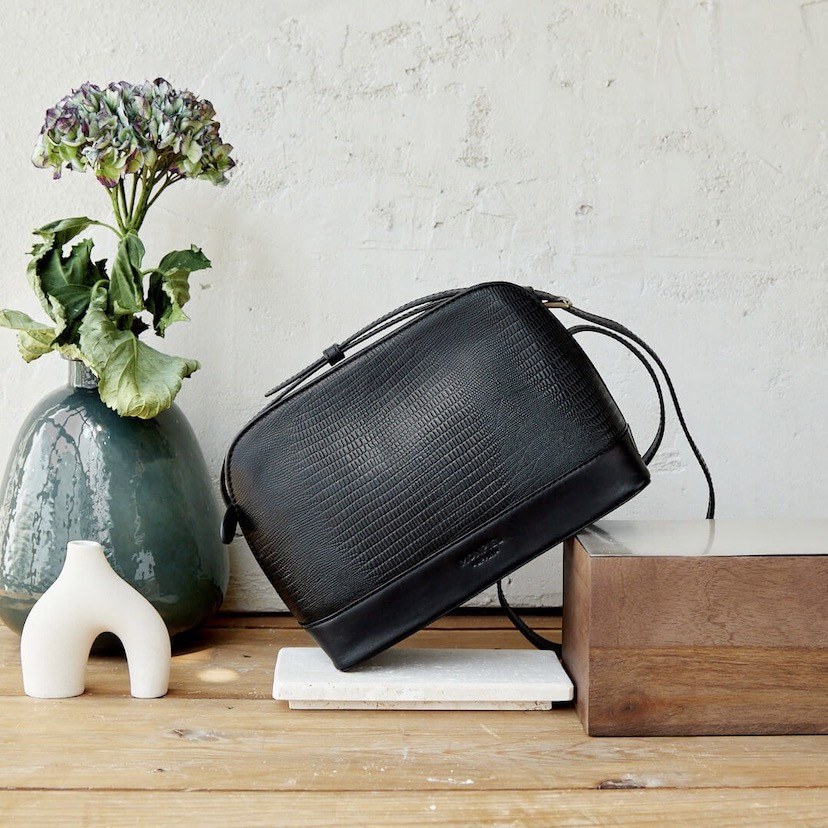 Medium leather bag in black snakeskin pattern, front view, tilted on wood - MONPIEL