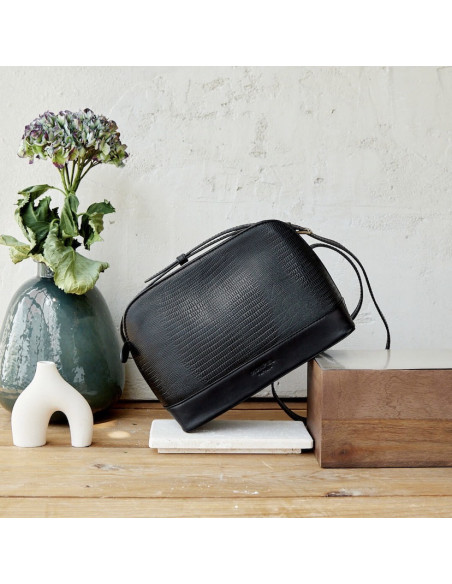 Medium leather bag in black snakeskin pattern, front view, tilted on wood - MONPIEL Medium leather bag in black snakeskin pattern, front view, tilted on wood - MONPIEL