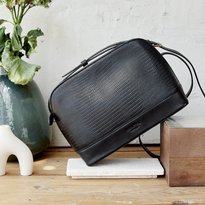 Medium leather bag in black snakeskin pattern, front view, tilted on wood, close-up - MONPIEL