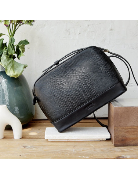 Medium leather bag in black snakeskin pattern, front view, tilted on wood, close-up - MONPIEL Medium leather bag in black snakeskin pattern, front view, tilted on wood, close-up - MONPIEL
