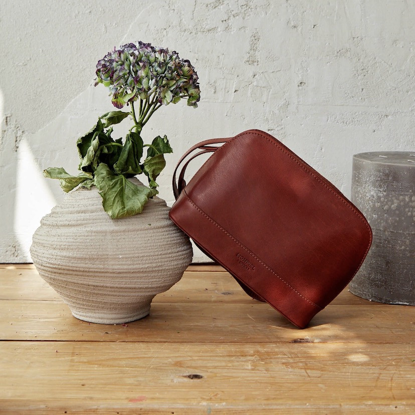 Medium leather bag in tan color, front view, tilted on a vase - MONPIEL