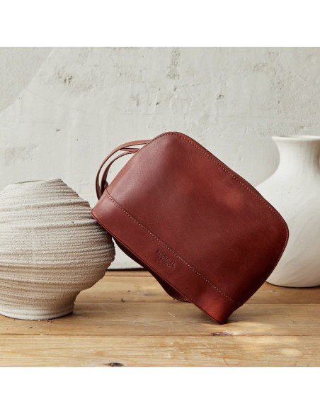 Bolsa média de couro em tom couro, vista frontal inclinada sobre um vaso em primeiro plano - MONPIEL Bolsa média de couro em tom couro, vista frontal inclinada sobre um vaso em primeiro plano - MONPIEL