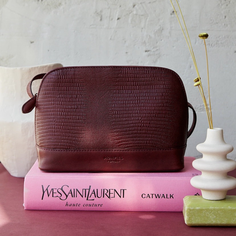 Medium leather bag in burgundy snakeskin pattern, front view, resting on a book - MONPIEL