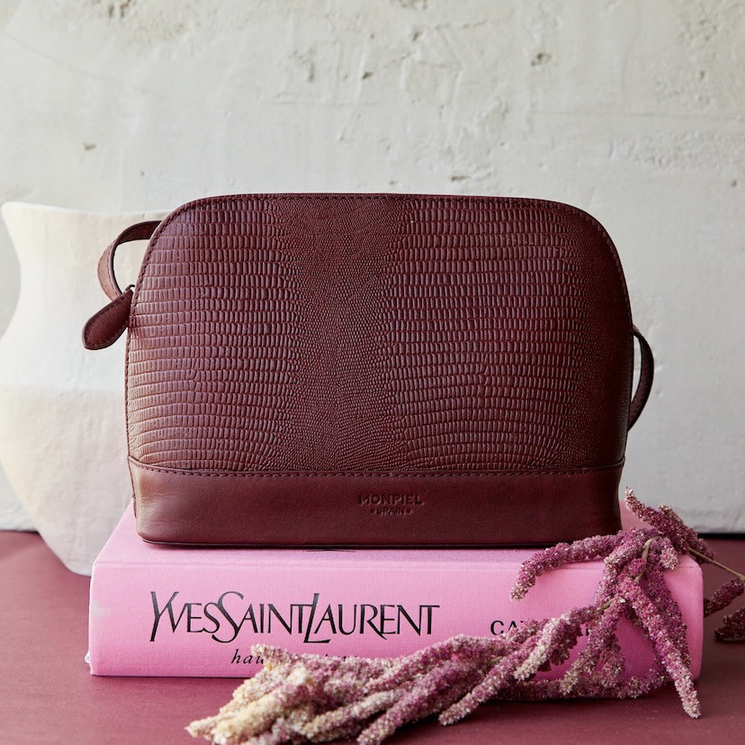 Medium leather bag in burgundy snakeskin pattern, front view, resting on a book with flowers - MONPIEL