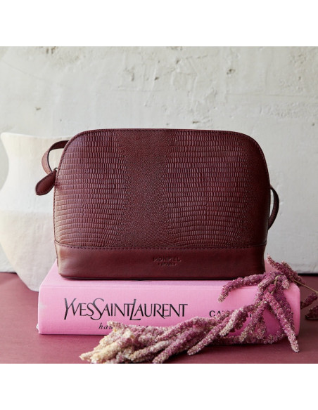 Medium leather bag in burgundy snake print, front view, resting on a book and flowers - MONPIEL