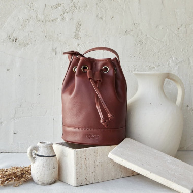 Bolsa saco bombonera pequena de couro em tom couro, vista frontal ao lado de um jarro - MONPIEL 2