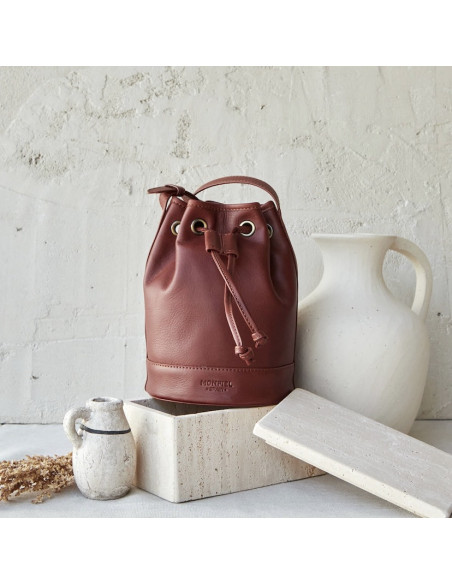 Small tan leather bucket bag, front view, next to a vase - MONPIEL Small tan leather bucket bag, front view, next to a vase - MONPIEL