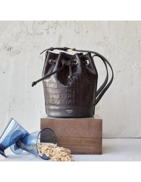 Small crocodile-patterned leather bucket bag in brown color, front view, resting on wood - MONPIEL