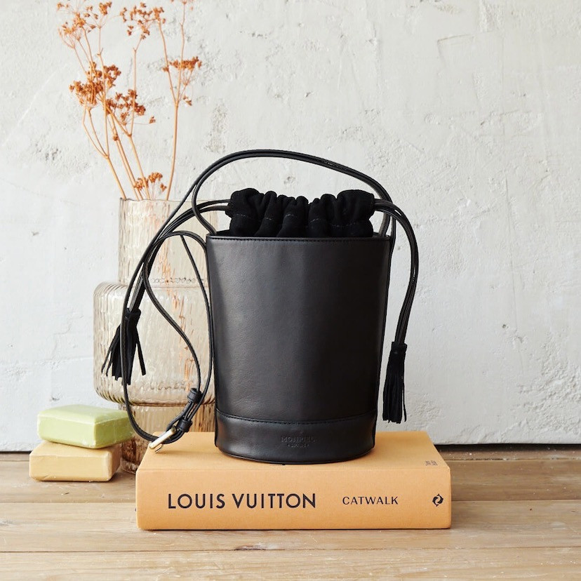 Small round bucket leather bag in black color, front view, resting on a book - MONPIEL