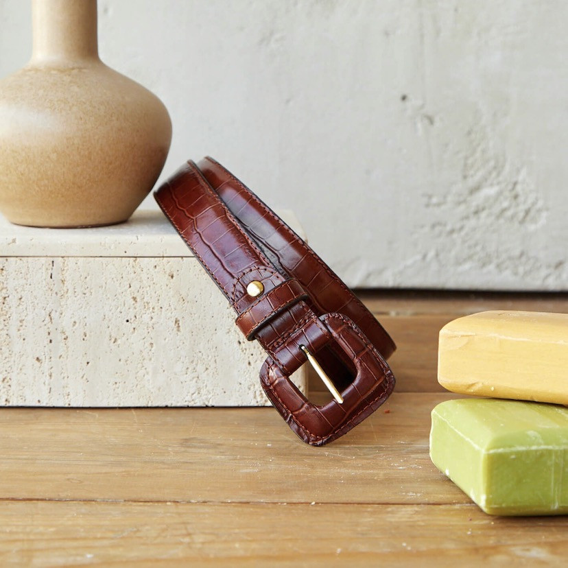 Women’s covered buckle belt with crocodile pattern in brown, coiled on marble next to soap - MONPIEL