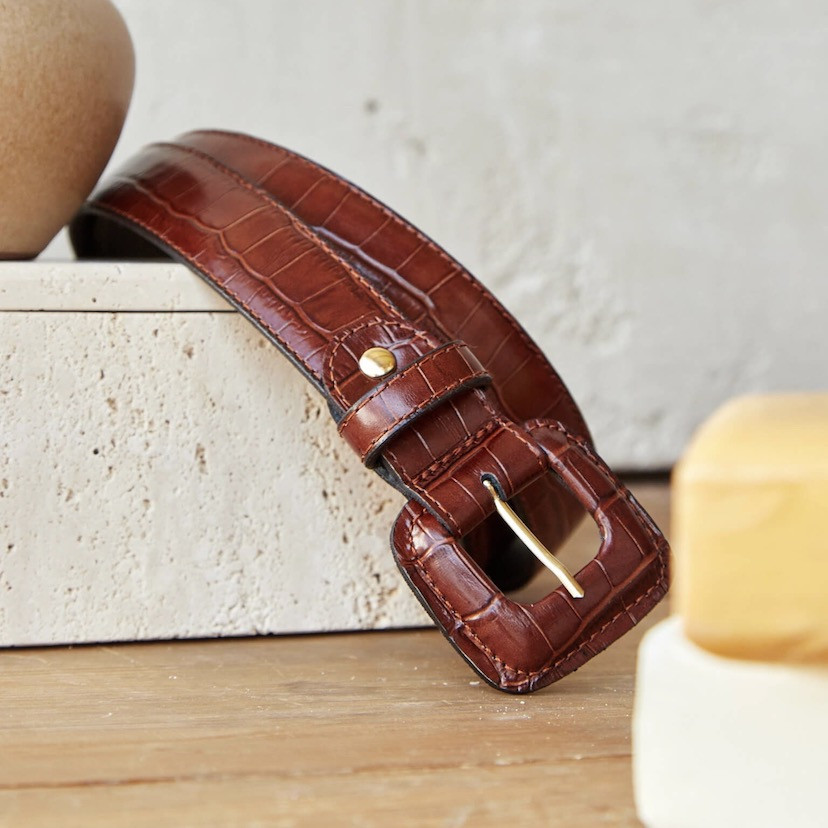 Women’s covered buckle belt with crocodile pattern in brown, coiled, close-up of buckle detail, on marble next to soap - MONPIEL