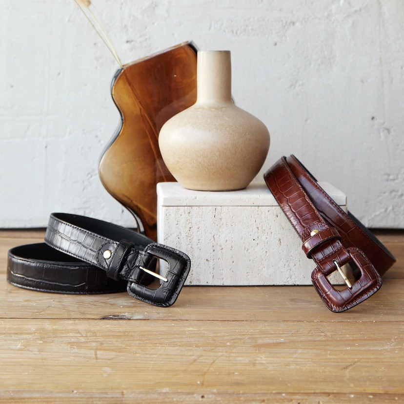 Women’s covered buckle belts with crocodile pattern in brown and black, coiled next to a vase - MONPIEL