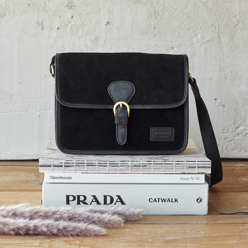Bolsa satchel com fivela em camurça preta, vista frontal apoiada em livros - MONPIEL