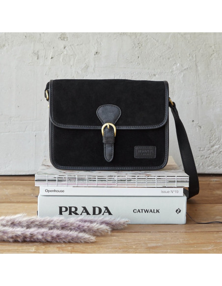 Black suede satchel bag with buckle, front view, resting on books - MONPIEL