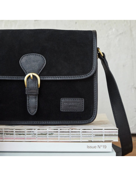 Bolsa satchel com fivela em camurça preta, vista frontal apoiada em livros, detalhe do logotipo - MONPIEL