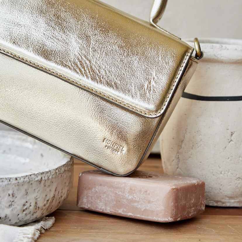Small Armado leather bag in metallic champagne color, tilted and resting on soap, logo detail - MONPIEL