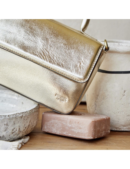 Bolsa pequena estruturada de couro metálico champanhe, inclinada apoiada sobre sabão com detalhe do logotipo - MONPIEL Bolsa pequena estruturada de couro metálico champanhe, inclinada apoiada sobre sabão com detalhe do logotipo - MONPIEL