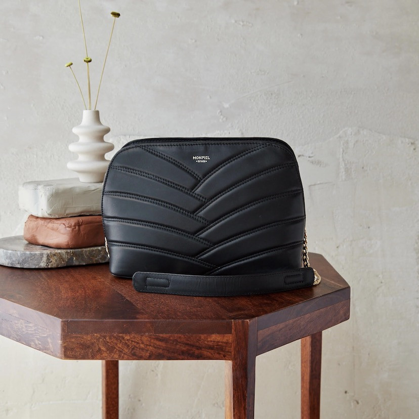 Bolsa acolchoada de couro com corrente dourada em preto, sobre mesinha, vista frontal - MONPIEL