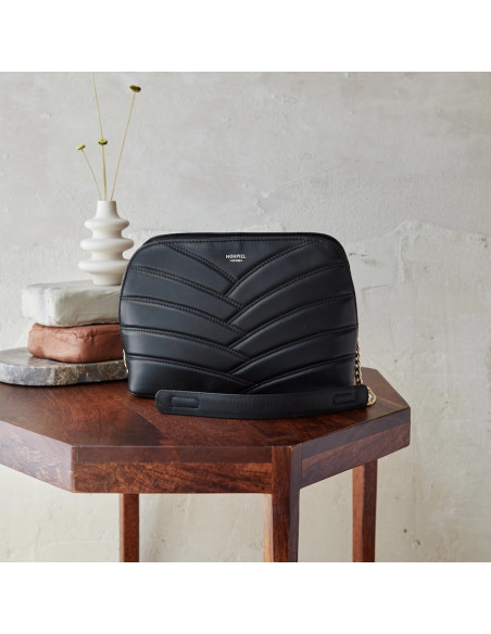 Schwarze gefütterte Ledertasche mit goldener Kette, auf einem kleinen Tisch, Frontalansicht - MONPIEL