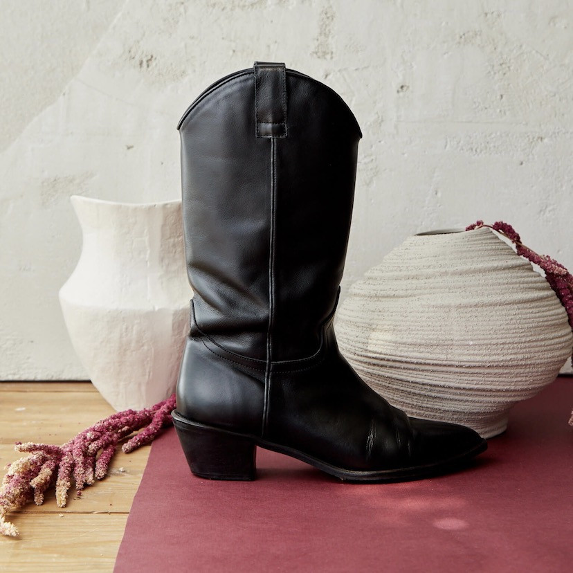 Mid-calf leather cowboy boot in black color, side view, next to vases - MONPIEL