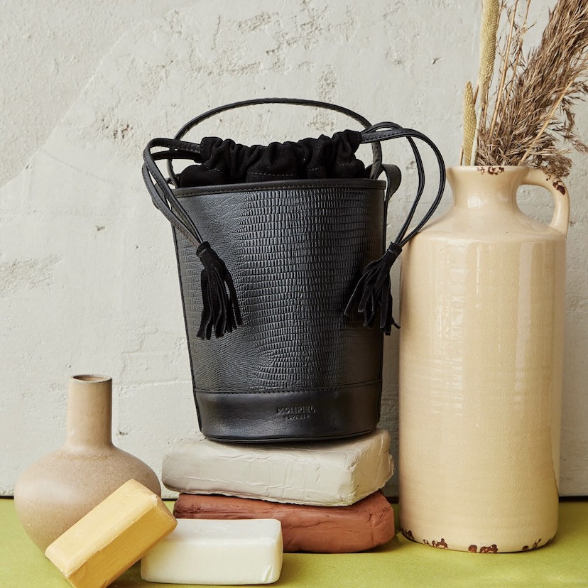 Bolsa redonda pequena de couro com estampa de cobra preta, vista frontal ao lado de um vaso - MONPIEL