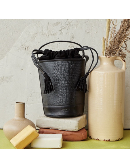Small black snake-pattern round leather bucket bag, front view, next to a vase - MONPIEL