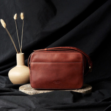 Black leather crossbody bag, front view slightly tilted, resting on a magazine - MONPIEL 2
