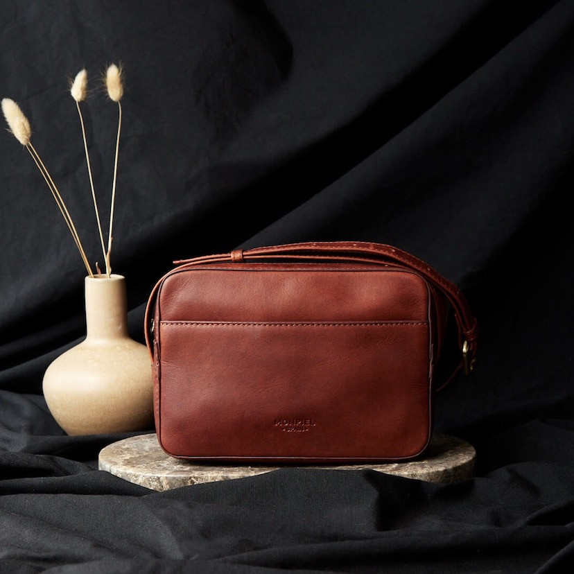 Bolsa tiracolo de couro em tom couro, vista frontal em fundo preto com detalhe de vaso - MONPIEL