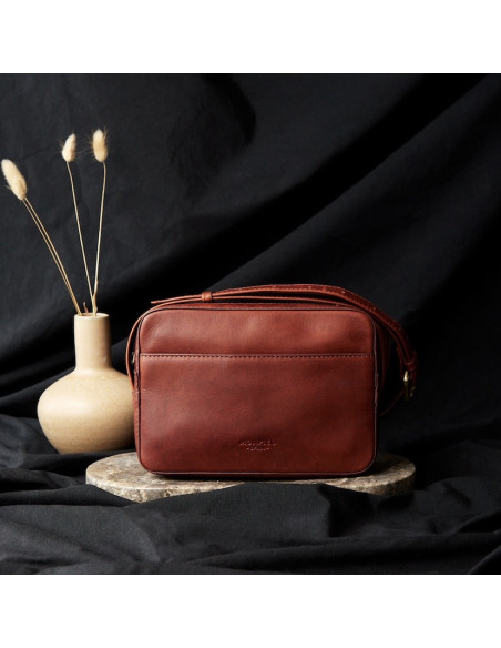 Sac bandoulière en cuir couleur cuir, vue de face, sur fond noir, avec détail d’un vase - MONPIEL Sac bandoulière en cuir couleur cuir, vue de face, sur fond noir, avec détail d’un vase - MONPIEL