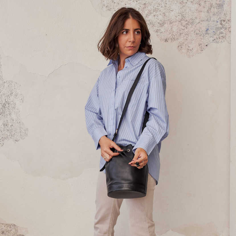 Large black leather bucket bag hanging from the shoulder, closure detail - MONPIEL
