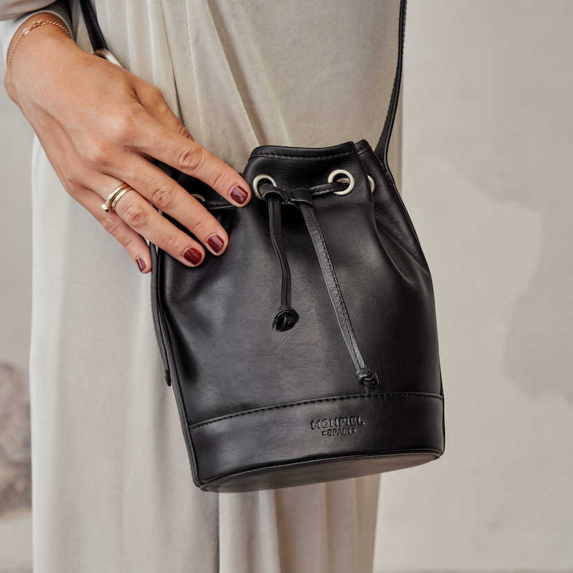 Bolsa bombonera pequena de couro preta, vista frontal com detalhe da mão - MONPIEL