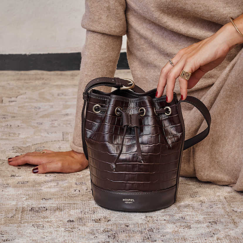 Bolsa bombonera pequena de couro marrom com estampa de crocodilo, apoiada no chão - MONPIEL