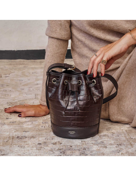 Bolso saco bombonera pequeño de piel en color marrón coco apoyado en el suelo - MONPIEL  Bolso saco bombonera pequeño de piel en color marrón coco apoyado en el suelo - MONPIEL