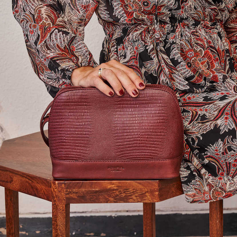 Bolsa média de couro bordô com estampa de cobra, vista frontal, apoiada na mesinha - MONPIEL