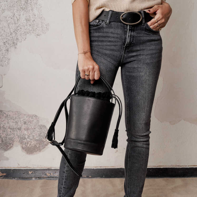 Cinto de couro preto com fivela oval, plano médio, segurando uma bolsa de couro preta - MONPIEL
