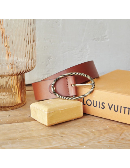 Tan leather belt with an oval buckle, coiled on a soap and a book - MONPIEL