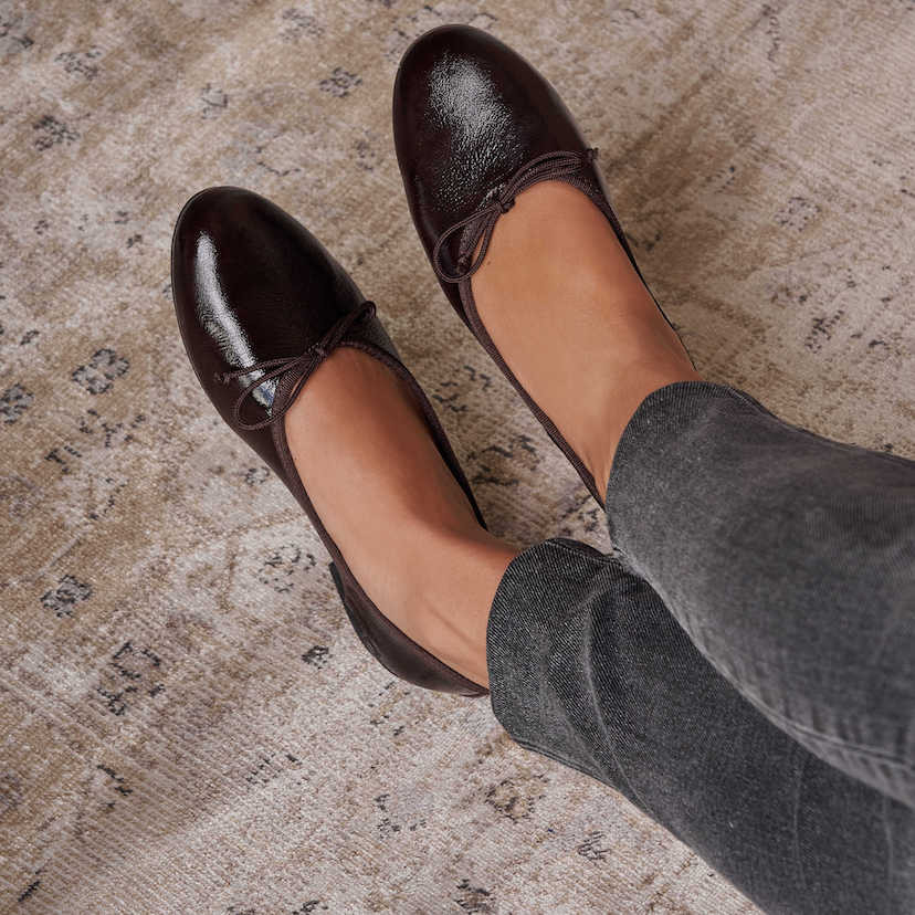 Brown patent leather high-heeled ballerina flats with crossed feet on a carpet - MONPIEL