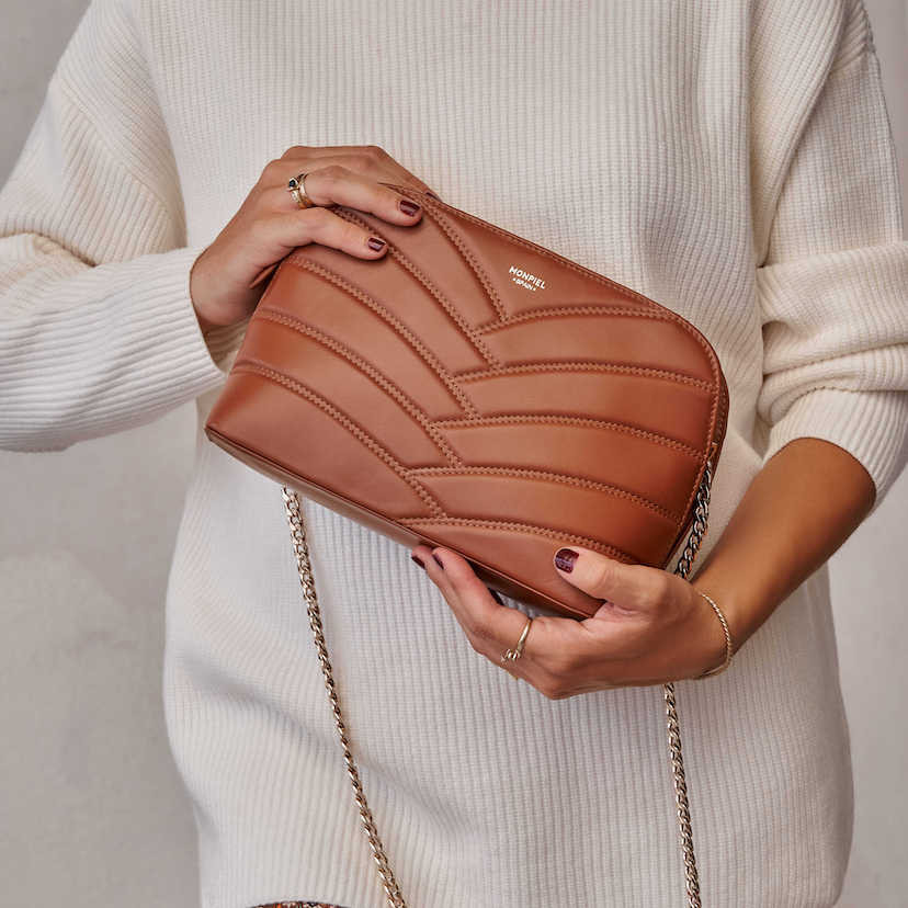 Bolsa acolchoada de couro marrom com corrente dourada, segurada nas mãos, inclinada - MONPIEL