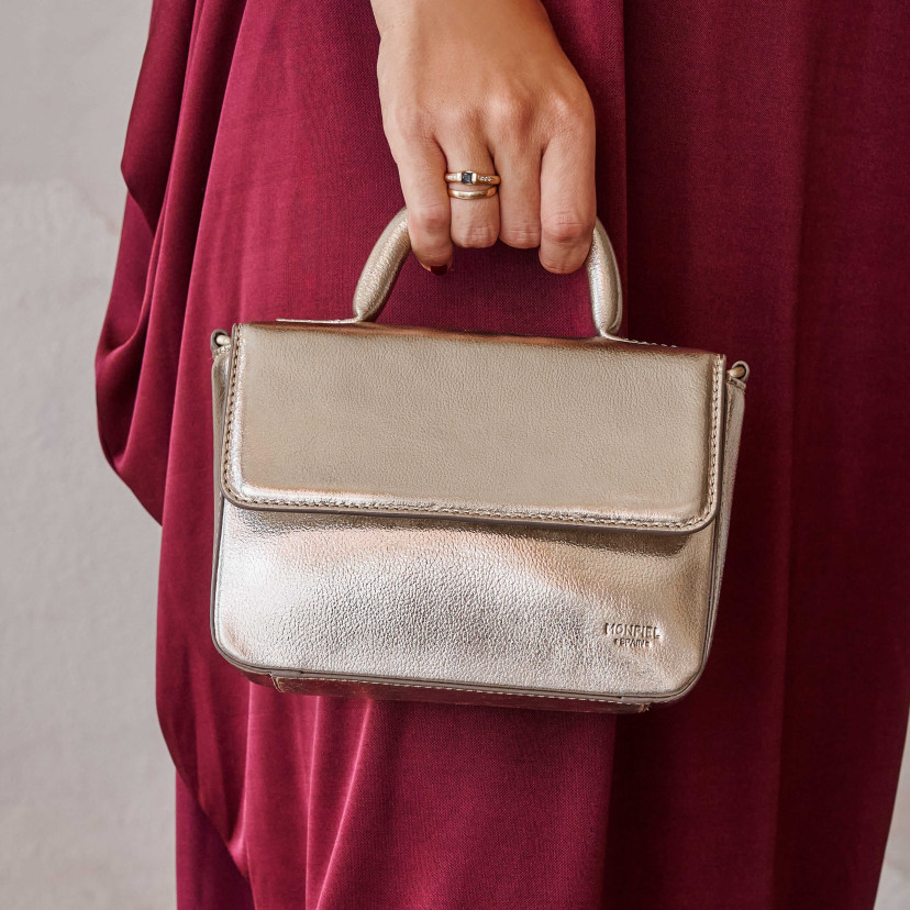 Bolsa pequena de couro metálico champanhe, vista frontal, segurada pela alça - MONPIEL