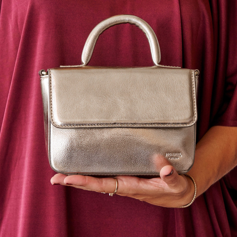 Bolsa pequena de couro metálico champanhe, vista frontal, apoiada na mão - MONPIEL