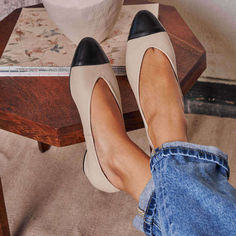 Beige leather bicolor pointed toe ballerina with front view, feet crossed, resting on a small table - MONPIEL