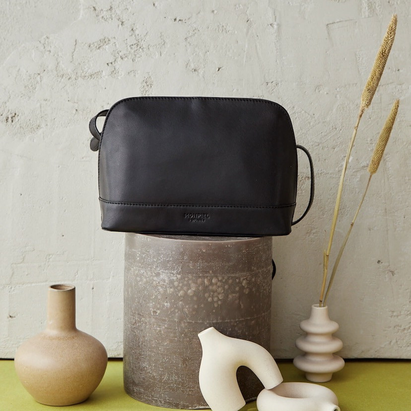 Medium black leather bag with front view, placed on top of a candle - MONPIEL