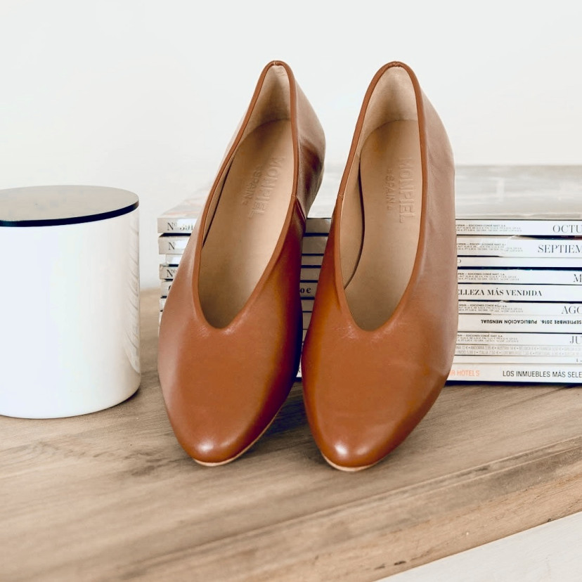 Flat leather ballerina in leather color, perspective view with the heel resting on magazines - MONPIEL