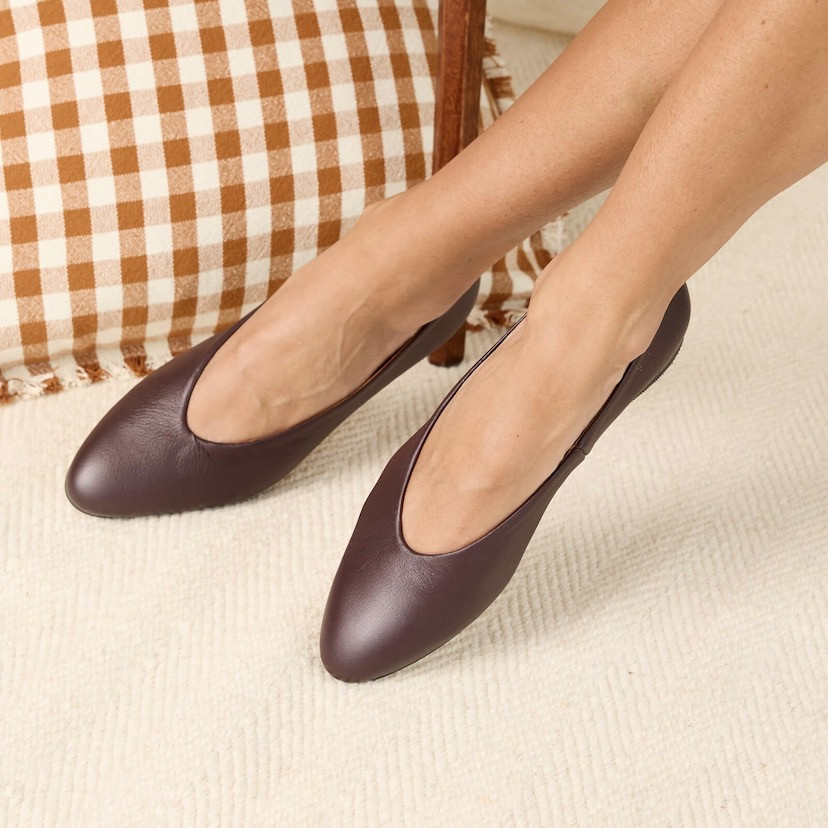 Burgundy flat ballerina, feet crossed with enlarged detail, and cushion in the background - MONPIEL