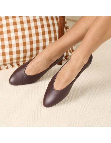 Ballerines plates couleur bordeaux, pieds croisés, détail en gros plan, avec un coussin en arrière-plan - MONPIEL