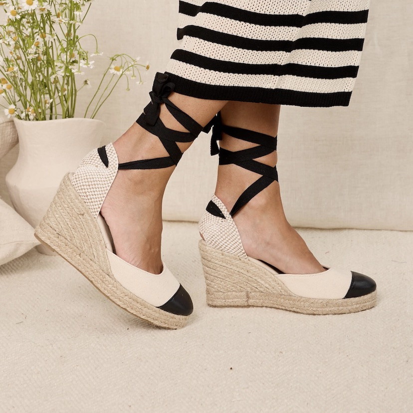 Black leather wedge espadrille with pointed toe, footsteps in the background with a vase of flowers - MONPIEL