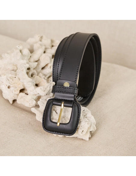 Ceinture femme en cuir noir avec boucle recouverte, enroulée avec un canapé en arrière-plan - MONPIEL